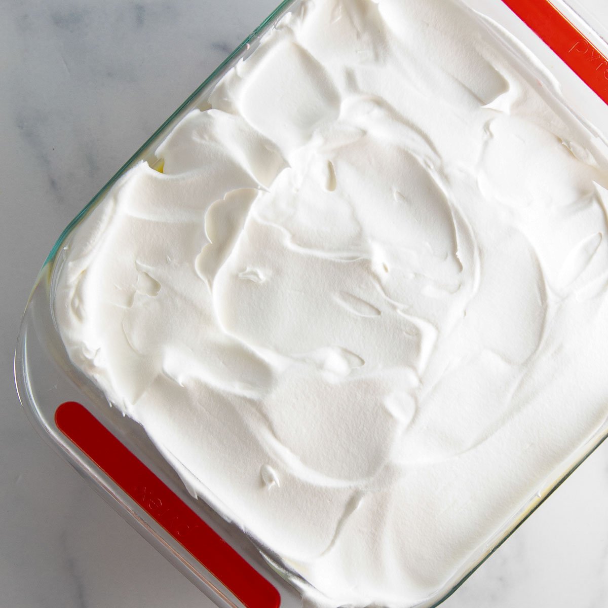 spreading cool whip over pudding layer in strawberry lasagna