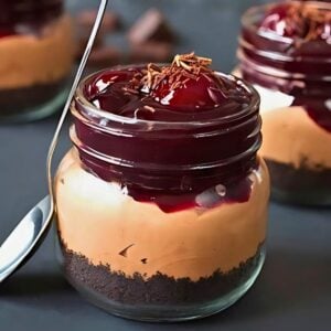 individual chocolate cherry cheesecakes in 8 ounce mason jars, garnished with black cherry pie filling and grated chocolate.