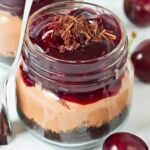 close-up of no bake chocolate cherry cheesecake in a mason jar with layers of oreo crust, chocolate filling and cherries.