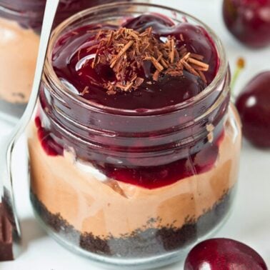 close-up of no bake chocolate cherry cheesecake in a mason jar with layers of oreo crust, chocolate filling and cherries.