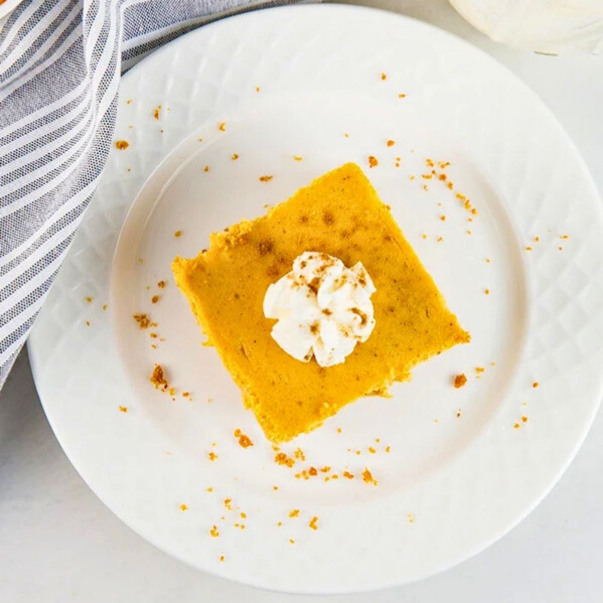 an overhead shot of pumpkin cheesecake bars cut into squares and served on a plate with whipped cream and pumpkin pie spice.