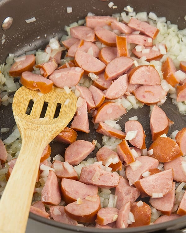 sliced sausage and onions cooking in a skillet