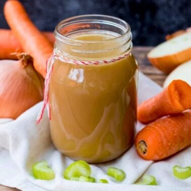 homemade chicken stock in a glass jar with vegetables in the background