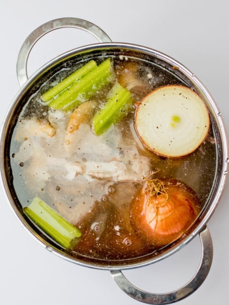 chicken stock simmering on the stove with vegetables and herbs.