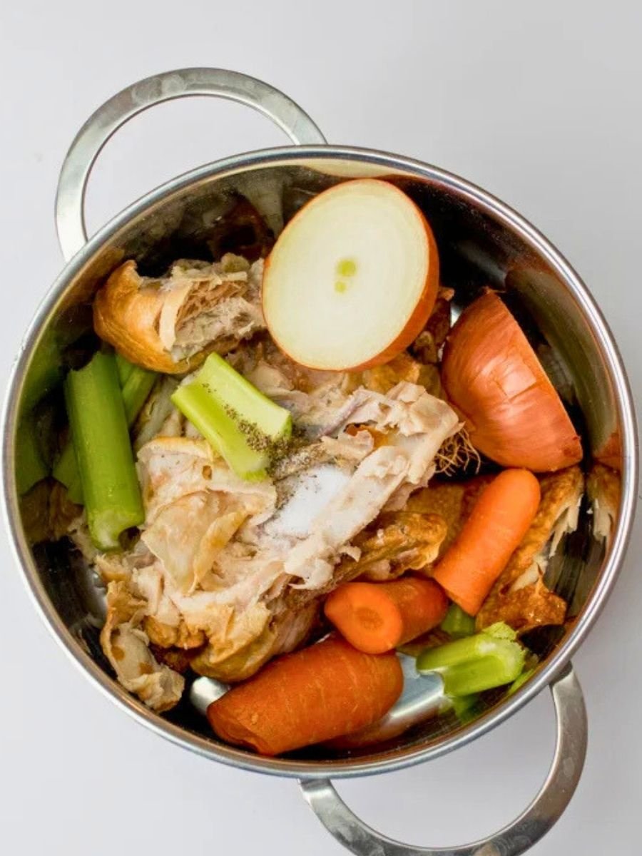 raw chicken bones, onions, carrots and celery arranged in a large stockpot before simmering to make chicken stock.
